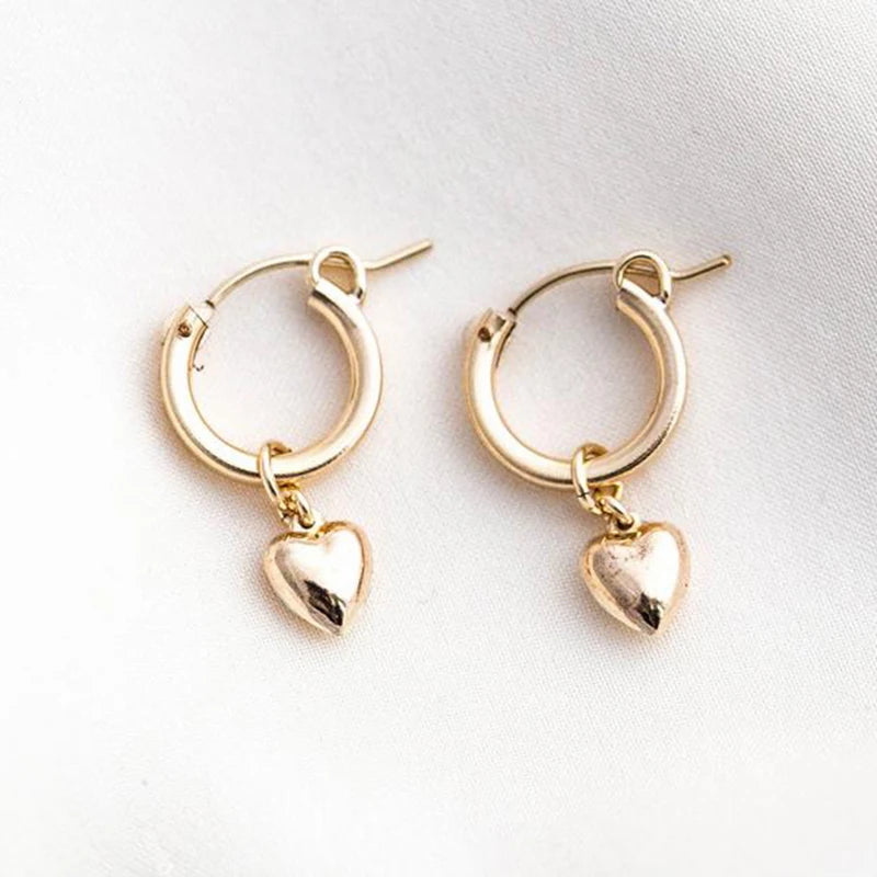 A pair of gold-filled hoop earrings with heart charms attached, displayed against a neutral background.
