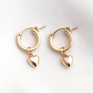 A pair of gold-filled hoop earrings with heart charms attached, displayed against a neutral background.